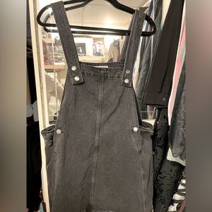 Black denim overall dress with button fasteners.